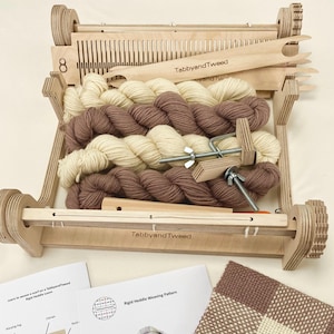 May include: A wooden weaving loom with a rigid heddle, two skeins of yarn in brown and cream, and a weaving pattern instruction sheet. The loom is labelled "TabbyandTweed".
