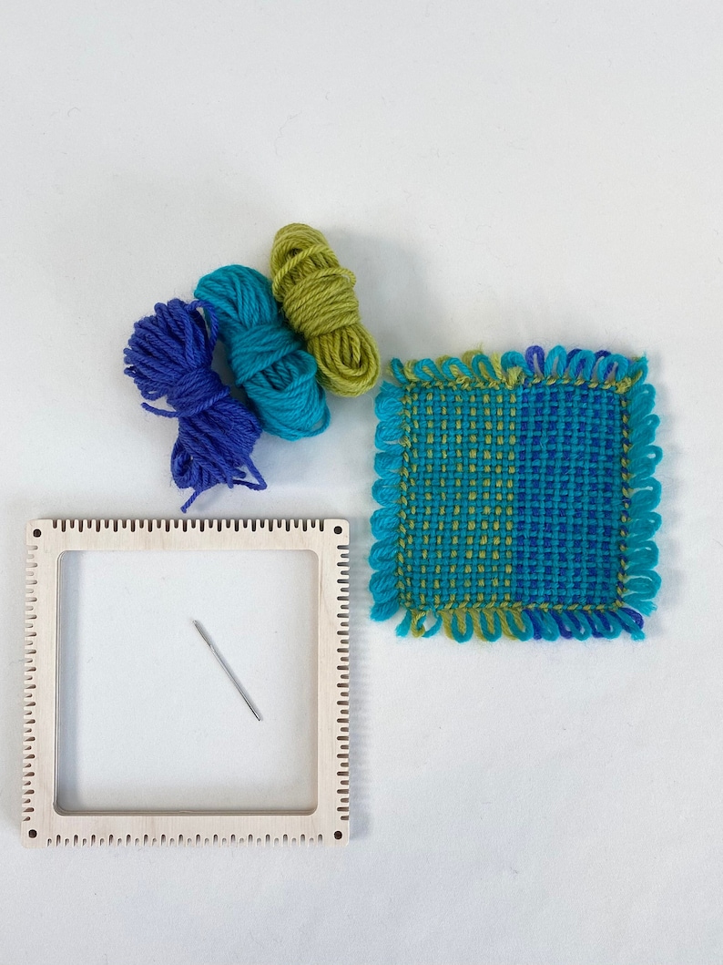 pinless pin loom with an example of a fabric square woven on the loom with balls of the wool used and tapestry needle.