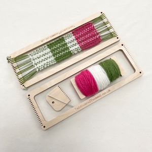 May include: A wooden weaving loom with a partially woven piece of fabric in green, white, and pink yarn. The loom is accompanied by a ball of yarn in the same colours and a weaving needle.