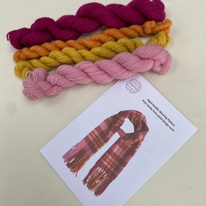 May include: A set of four skeins of yarn in pink, orange, yellow, and burgundy colors. The yarn is arranged in a stack, with the burgundy yarn on top. The yarn is labeled "Nordic Heddle Weaving Pattern Pink Candy Floss plaid design scarf".