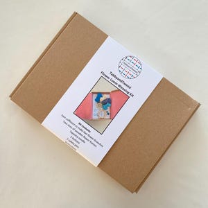 May include: A brown cardboard box with a white label that says "TabbyandTweed Flower Loom Weaving Kit". The label also includes a list of kit contents: yarn, two sizes of wooden flower frames, a tapestry needle, two buttons, two safety pins, and instructions.
