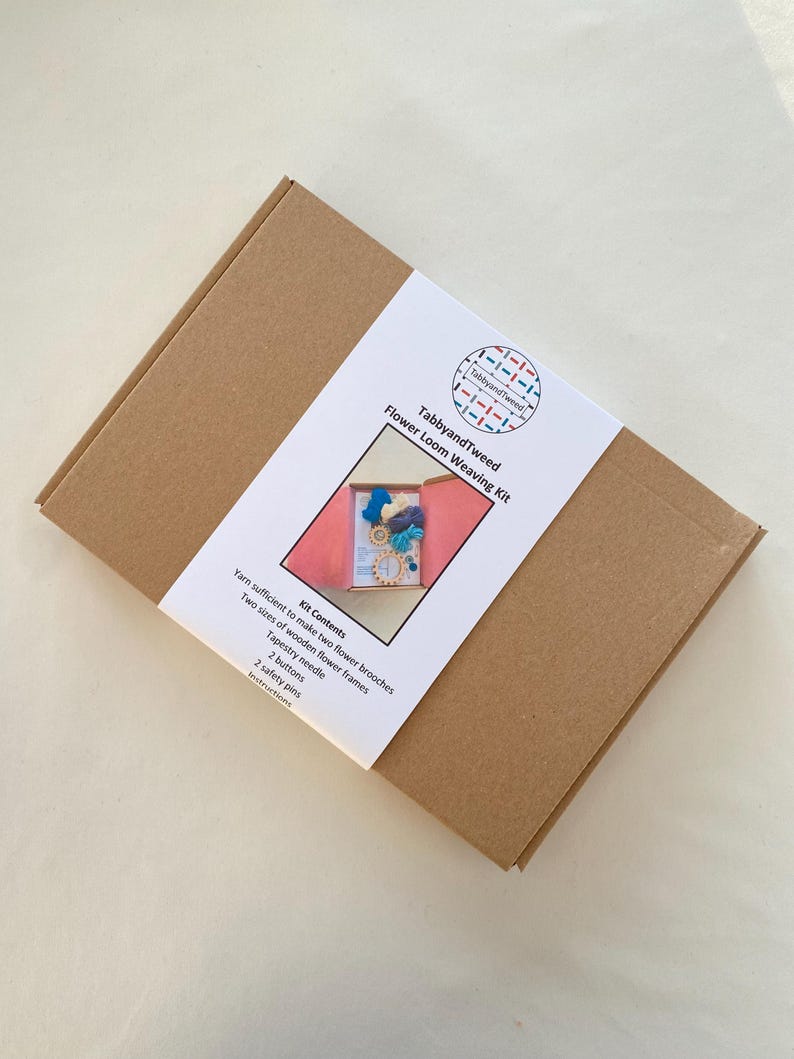 May include: A brown cardboard box with a white label that says "TabbyandTweed Flower Loom Weaving Kit". The label also includes a list of kit contents: yarn, two sizes of wooden flower frames, a tapestry needle, two buttons, two safety pins, and instructions.