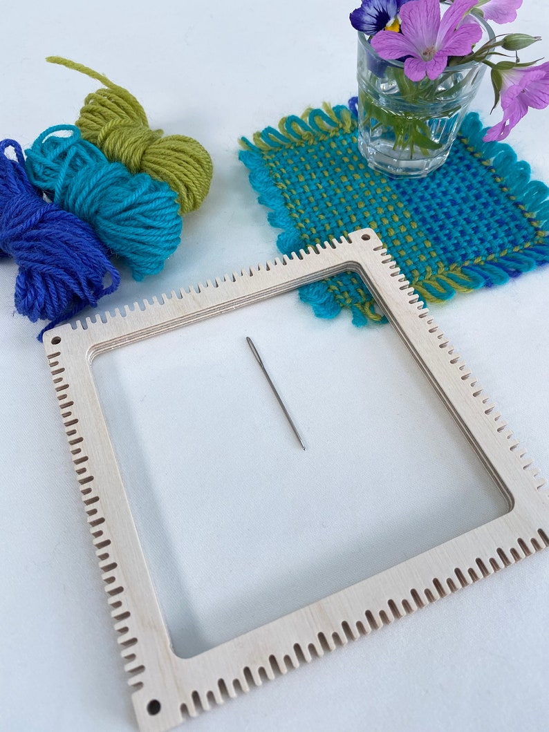 pinless pin loom with an example of a fabric square woven on the loom with balls of the wool used and tapestry needle.