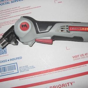 May include: A gray and black Craftsman Nextec cordless rotary tool with a red trigger. The tool has a black and gray handle and a silver metal bit attachment.