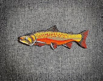 May include: A brown and orange embroidered patch of a trout fish with yellow spots.