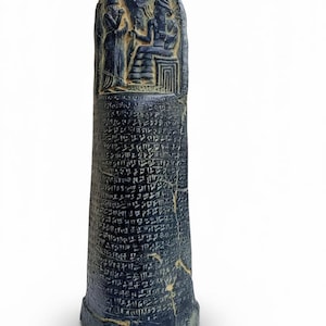 May include: A dark blue, ancient stone stele with carved figures at the top and cuneiform writing covering the majority of the surface. The stele has a slightly rounded top and a triangular base.