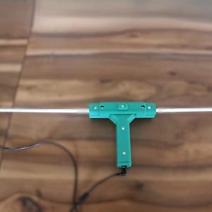 May include: A silver metal antenna with a teal handle and a teal power supply box. The antenna is T-shaped with a long horizontal bar and a vertical handle. The power supply box is rectangular with a fan.