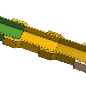 Puede incluir: Corte transversal de un objeto alargado multicolor. El objeto es principalmente amarillo, con una sección verde en un extremo y una sección beige en el otro. El objeto tiene forma rectangular con un interior hueco.