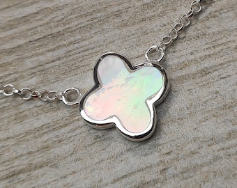 Op de afbeelding: Een zilveren ketting met een witte, iriserende klavertjevier-hanger.