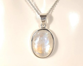 May include: A silver necklace with an oval moonstone pendant. The moonstone has a pearly white and yellow iridescent glow. The pendant is set in a silver bezel and hangs from a delicate silver chain. The necklace is displayed on a white mannequin.