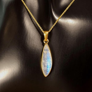 May include: A gold chain necklace with a pearlescent moonstone pendant. The pendant is a teardrop shape and has a subtle iridescent shimmer.