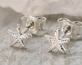 May include: A pair of silver starfish stud earrings. The earrings are small and delicate, and they have a textured finish.