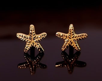 May include: A pair of gold-tone starfish stud earrings. The earrings are small and delicate, and they have a textured surface.