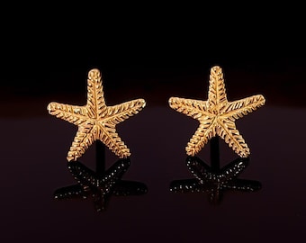 May include: A pair of gold-tone starfish stud earrings. The earrings are small and delicate, and they have a textured surface.