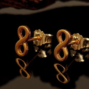 Op de afbeelding: Een paar gouden oorbelletjes in de vorm van een oneindigheidssymbool. De oorbelletjes zijn klein en delicaat en perfect voor dagelijks gebruik.