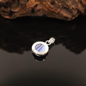 May include: A round, silver pendant with a blue and white iridescent stone center. The pendant has a simple, elegant design, perfect for everyday wear. The stone has a unique, swirling pattern.