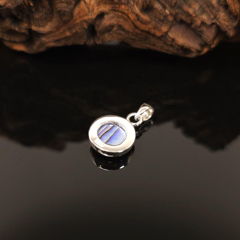 May include: A round, silver pendant with a blue and white iridescent stone center. The pendant has a simple, elegant design, perfect for everyday wear. The stone has a unique, swirling pattern.
