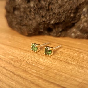May include: A pair of small, round, green gemstone earrings with gold settings and silver posts.