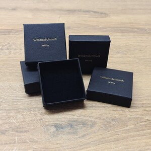 Puede incluir: Cuatro cajas cuadradas negras con el texto "WilliamsSchmuck bei Etsy" impreso en dorado en la parte superior de cada caja.