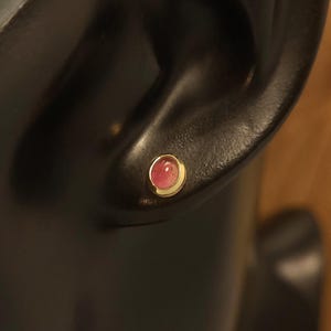Puede incluir: Primer plano de un pendiente de piedra rosa con engaste de oro. El pendiente se lleva en la oreja de un maniqu&iacute;.