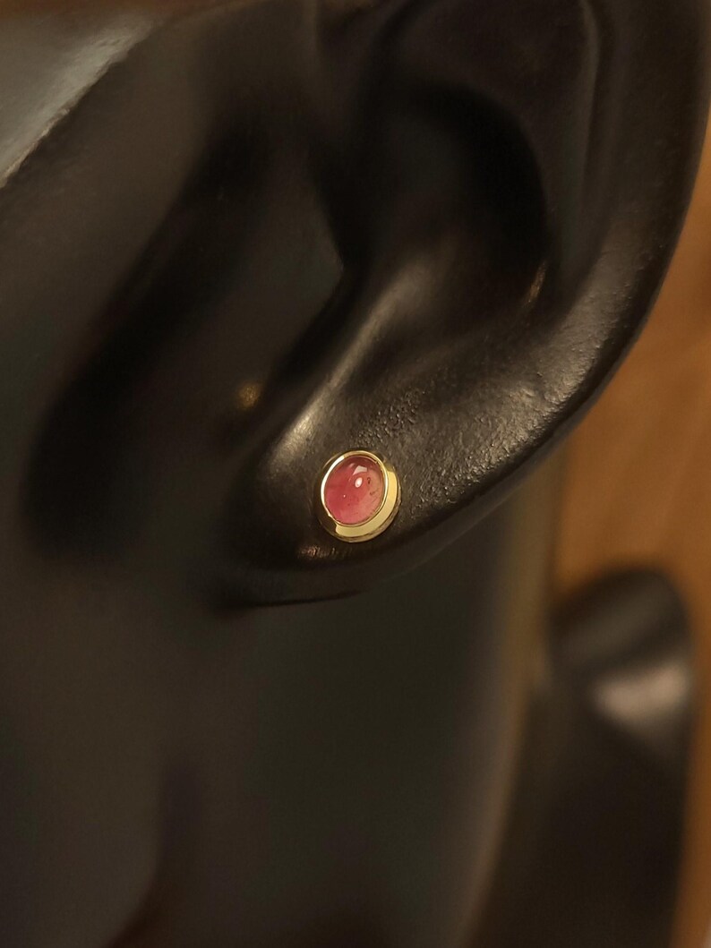 Puede incluir: Primer plano de un pendiente de piedra rosa con engaste de oro. El pendiente se lleva en la oreja de un maniqu&iacute;.
