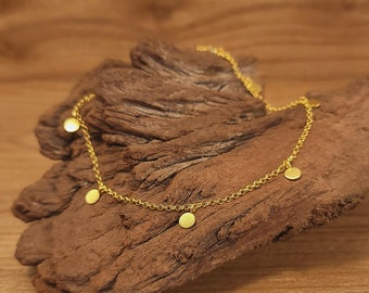 May include: A gold chain necklace with small, round gold charms hanging from it. The necklace is on a piece of wood.