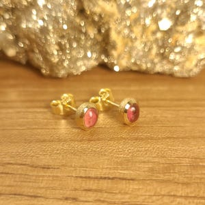 Puede incluir: Un par de pendientes de oro con piedras preciosas rosas. Los pendientes est&aacute;n sobre un fondo de madera.