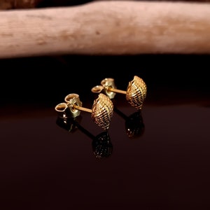 May include: A pair of gold-toned earrings with a textured, shell-like design. The earrings are small and delicate.