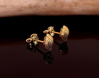 May include: A pair of gold-toned earrings with a textured, shell-like design. The earrings are small and delicate.