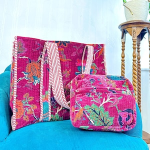 Op de afbeelding: Twee gestikte stoffen tassen met bloemenpatronen. De grotere tas heeft witte en rode gestreepte banden. De kleinere tas is een compactere stijl. Beide tassen zijn roze met groene en oranje bloemenontwerpen.