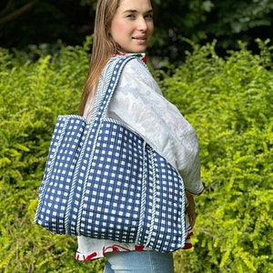 Könnte beinhalten: Eine blaue und weiße Gingham-Tragetasche mit weißen Seilgriffen. Die Tasche ist aus gestepptem Stoff und hat eine leicht strukturierte Oberfläche.
