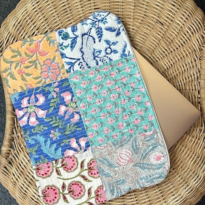 May include: A patchwork laptop sleeve with a floral design in shades of blue, green, pink, and yellow. The sleeve is made of cotton and has a zipper closure.