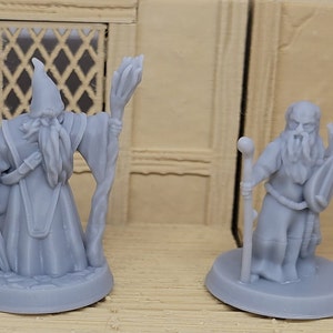 May include: Two gray 3D printed figurines of wizards. The wizard on the left is holding a staff and a sword. The wizard on the right is holding a staff and a lute.