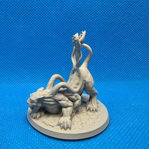 May include: A gray, 3D-printed monster figurine with multiple tentacles and a detailed, textured surface. The creature is posed on a circular base, set against a blue background. The figurine has a menacing expression.