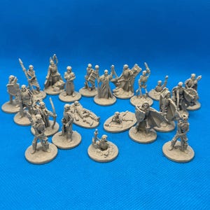 May include: A collection of 18 unpainted plastic miniature skeletons in various poses, including standing, kneeling, and lying down. The skeletons are arranged on a blue surface.