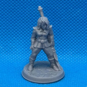 May include: A gray miniature figurine of a female warrior, posed with a sword and a long object on her back. The figure is standing on a circular base. The warrior is wearing a tunic and boots.