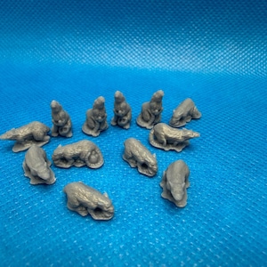 May include: A collection of small, gray animal figurines, possibly polar bears, are scattered on a textured blue surface. The figurines are in various poses, some standing, some lying down, and some sitting.