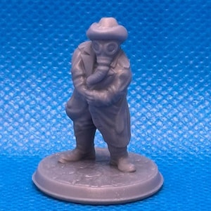 May include: A gray miniature figurine of a person wearing a gas mask, hat, and long coat. The figure is standing on a circular base. The overall design suggests a post-apocalyptic or dystopian theme.