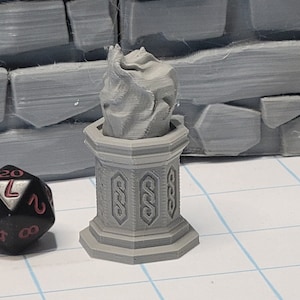 May include: A gray, 3D printed miniature of a stone pedestal with a sculpted flame on top. The pedestal has intricate details and a square base.
