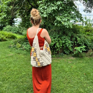 May include: A woman wearing a red dress carries a crocheted tote bag with a geometric pattern in beige, yellow, and gray.