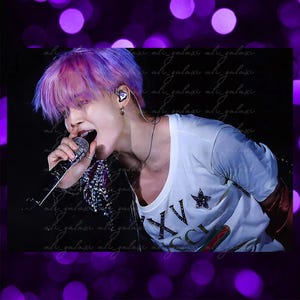 May include: A person with pink and purple hair singing into a microphone. They are wearing a white t-shirt with a star and the letters "XV" and "GUCCI" printed on it. The background is dark with a purple bokeh effect.