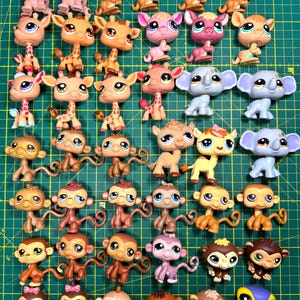 Puede incluir: Una colección de pequeñas figuras de animales de plástico de colores, incluyendo monos, jirafas, elefantes y otras criaturas. Los juguetes están dispuestos sobre una esterilla de corte verde, mostrando una variedad de diseños y colores.