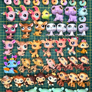 May include: A collection of various Littlest Pet Shop animal figurines arranged on a green cutting mat with a grid. The set includes seahorses, monkeys, giraffes, seals, and other creatures with large eyes, displayed in rows against the grid lines.