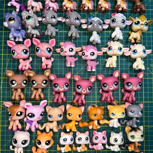 Puede incluir: Una colección de pequeñas figuras de animales de plástico de colores, incluyendo gatos, perros, ciervos y caballos. Los juguetes son de varios colores, con ojos grandes y detalles. Las figuras están dispuestas sobre una cuadrícula verde.