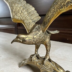 May include: A gold-toned brass eagle sculpture with outstretched wings, perched on a tree branch base. The eagle's feathers are intricately detailed, and its talons are gripping the branch.