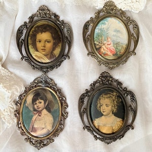 Op de afbeelding: Vier sierlijke, goudkleurige frames met glazen panelen, elk met een portret van een kind. De frames hebben ingewikkelde krulwerk en zijn in een vierkant patroon gerangschikt.