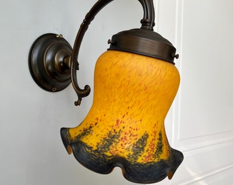 May include: A vintage-style wall sconce with a bronze finish and a yellow glass shade with black and red accents. The shade has a ruffled edge.