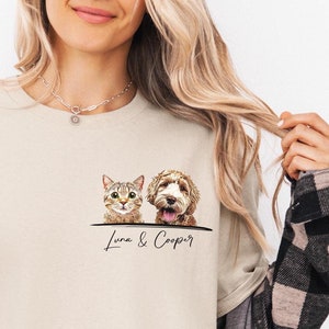 May include: A beige t-shirt with a graphic of a cat and a dog peeking over the top. The text "Luna & Cooper" is printed below the graphic.