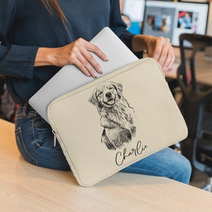 May include: Beige laptop sleeve featuring a black and white sketch of a Golden Retriever with the name "Charlie" in cursive. The sleeve is held with a silver laptop.