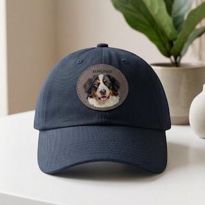 May include: A navy blue baseball cap with a circular patch displaying a dog portrait. The patch has the name "Bruno" above the dog's image. The dog has brown, black, and white fur.
